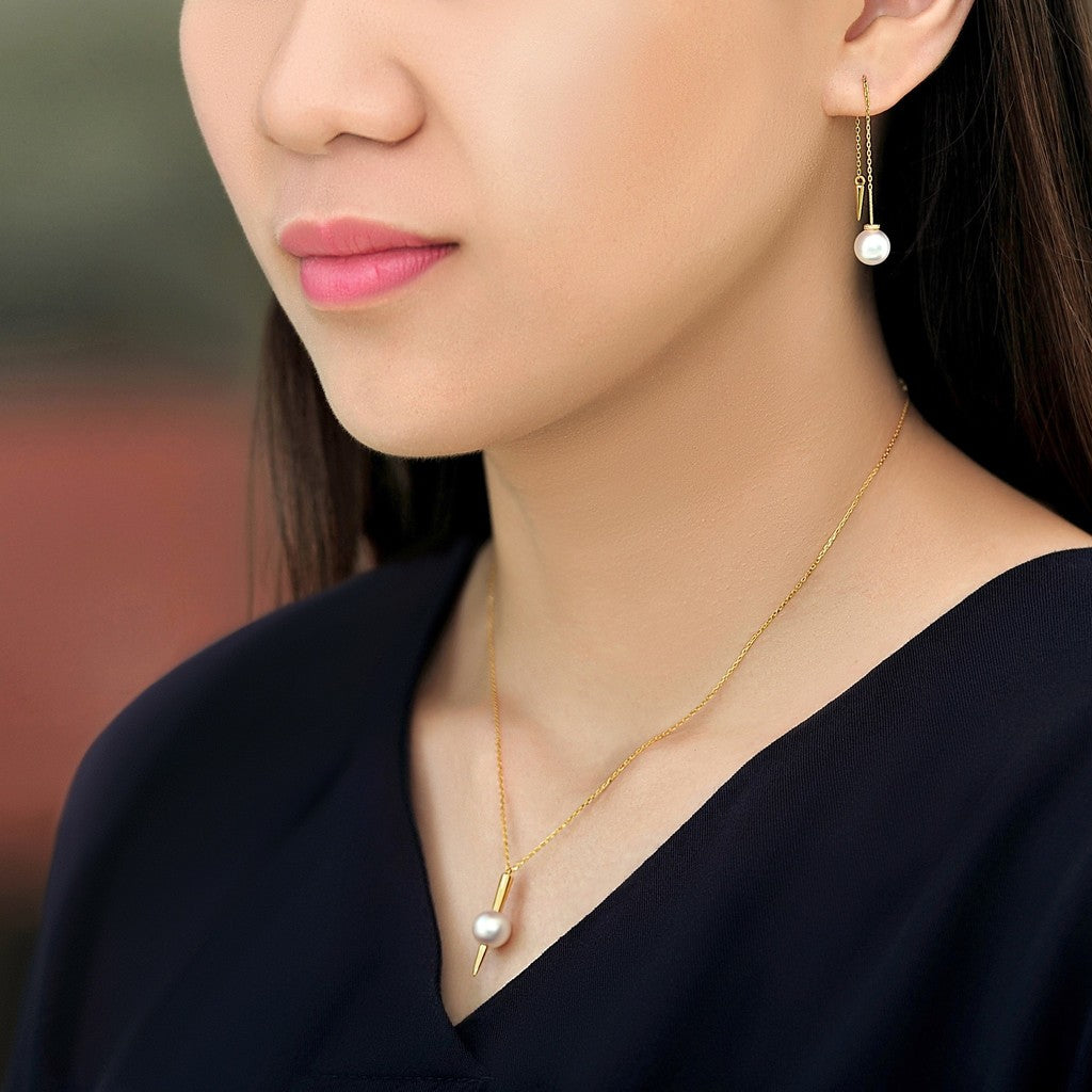 Model wearing a pair of Qlassico dangling earrings and pendant necklace from the  Celestial Capsule, featuring a pair of round Akoya pearls and a round Akoya pearl set in 18K yellow gold with a sculptural pointed design.