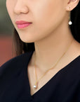Model wearing a pair of Qlassico dangling earrings and pendant necklace from the  Celestial Capsule, featuring a pair of round Akoya pearls and a round Akoya pearl set in 18K yellow gold with a sculptural pointed design.