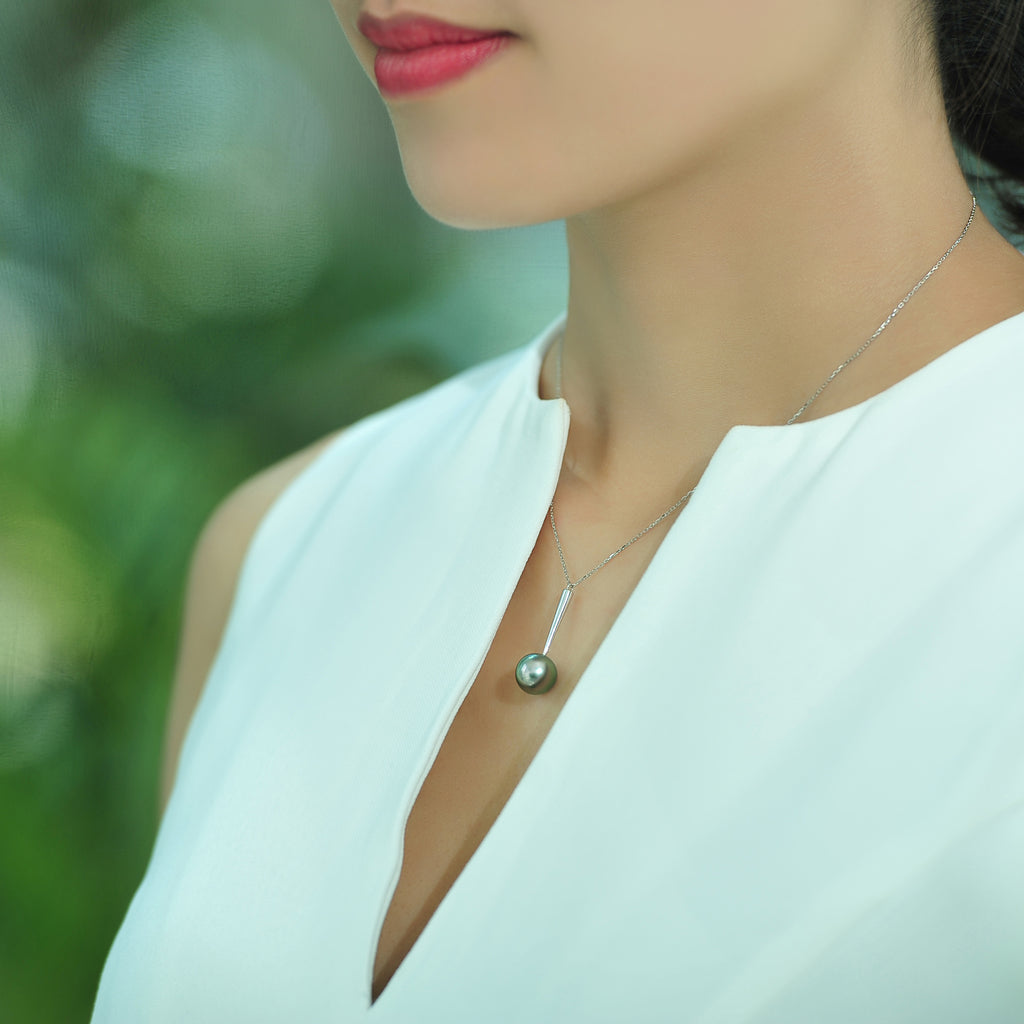 Model wearing a Qlassico pendant necklace from the Celestial Capsule, featuring a round peacock-coloured Tahitian pearl set in 18K white gold.
